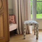 Le tabouret Mary en tissu rayé fleuri près d’une porte-fenêtre