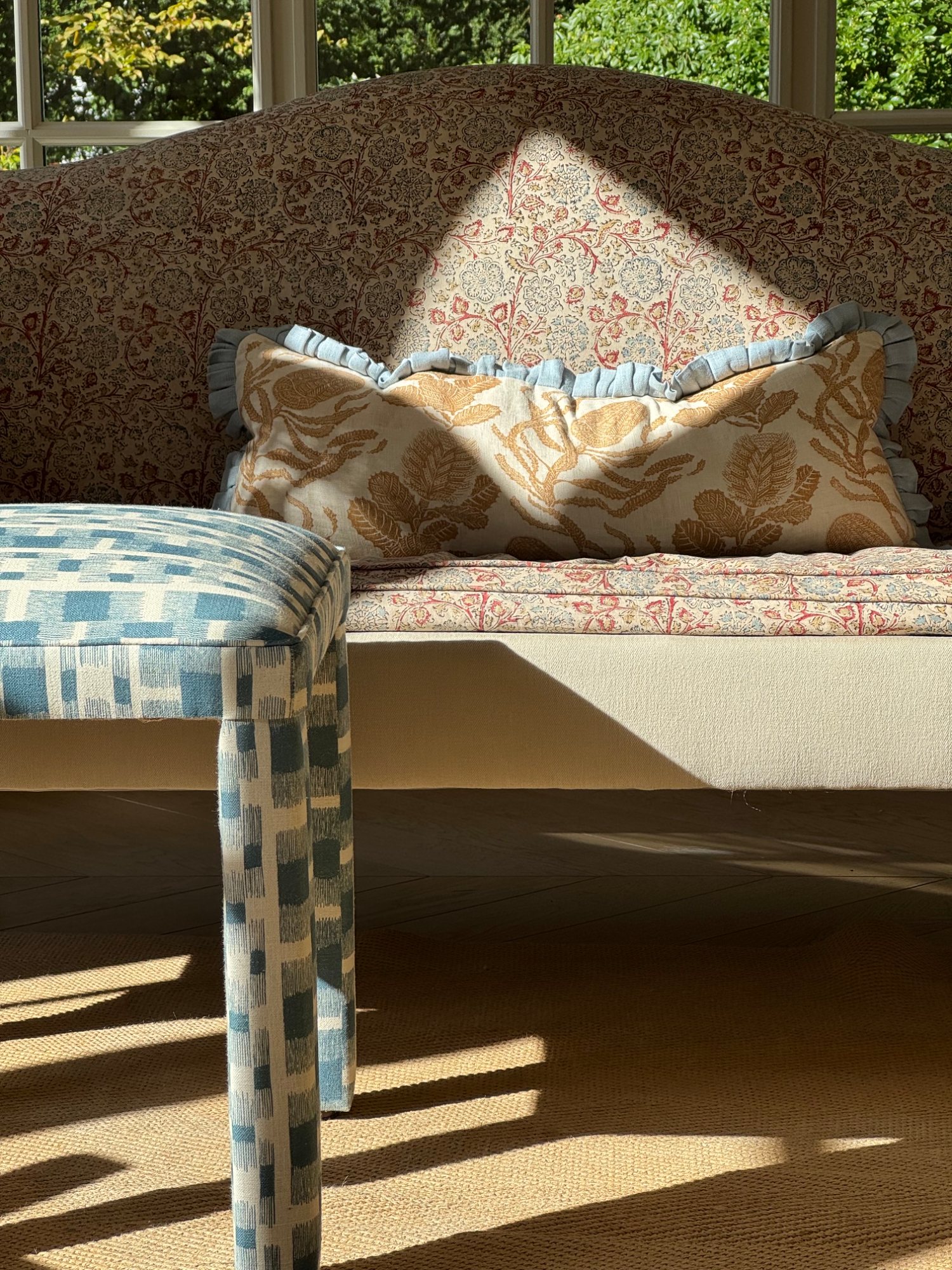 Le tabouret Mary en tissu ikat bleu devant un canapé fleuri