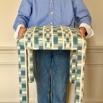 Tabouret Mary tapissé d’un tissu vert et écru, tenu à bout de bras